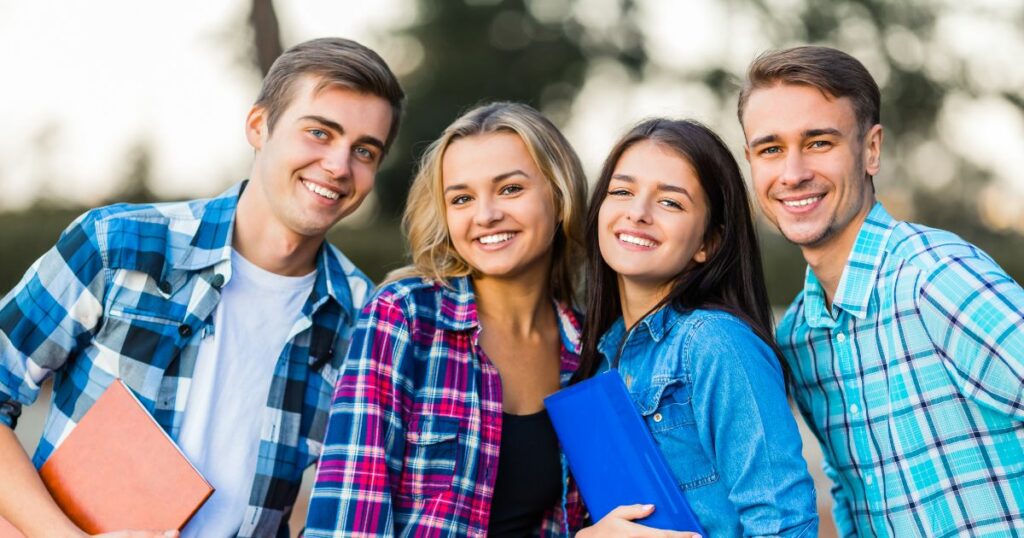 Grupa uśmiechniętych studentów z zeszytami w dłoniach – radosne odliczanie do wakacji dla studentów po sesji egzaminacyjnej